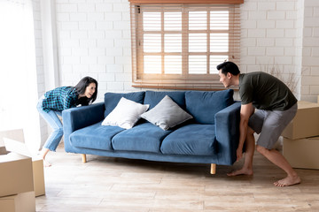 An Asian couple, husband and attractive wife, are helping to lift for moving the sofa in their new...