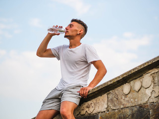 Young Caucasian man resting and drinking water after an outdoors workout