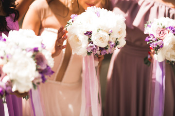 Bride with bridesmaids holding wonderful luxury wedding bouquet of different flowers on the wedding day