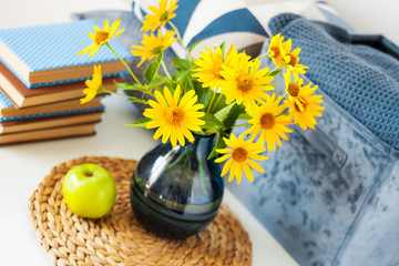 Cozy home interior decor: stack of books, green apple, decorative pillows, box with plaid and vase with yellow flowers on a glass table. Distance home education.Quarantine concept of stay home.