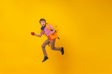Fototapeta na wymiar active schoolboy with a backpack, books and an Apple runs on a yellow background