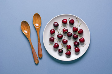 pile of cherries in plate with spoons beside - closeup