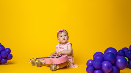 little baby playing guitar on yellow background with balloons in form of grapes