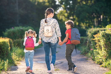 mother accompanies students on road. children with briefcases walk from school