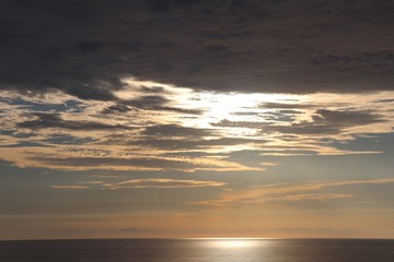 Gold twilight sky with clouds hiding the sun over a smooth glistening ocean