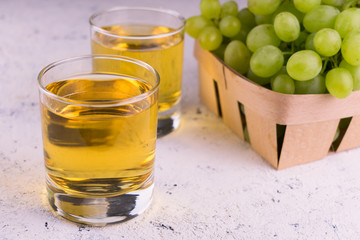 Two glasses with grape juice and a bunch of grapes on a white background.