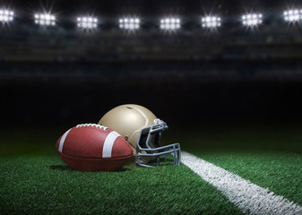 Football and helmet on grass field below stadium lights at night