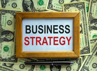 Wooden picture frame with inscription 'business strategy' on beautiful background from dollar bills...