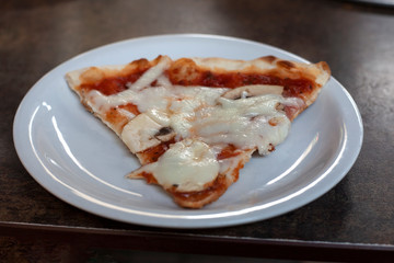 There is a slice of pizza on the table in the cafe. It is triangular in shape. It is in a white plate.