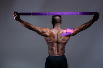 Rear view african american bodybuilder with kinesio tape on the shoulder joint raises his arms up