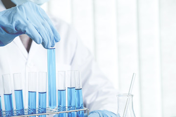 Scientists hold a glass tube filled with blue chemical liquid for research and analysis in a...