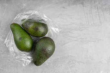 Top view of plastic or polyethylene transparent bag full of ripe green avocado on concrete gray...