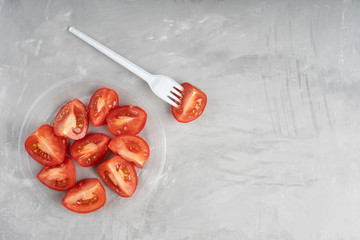 Plastic plate full of ripe tomato slices on concrete gray background together with polyethylene...