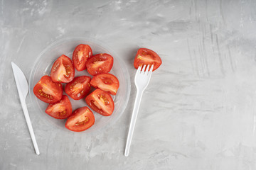 Plastic plate full of ripe tomato slices on concrete gray background together with polyethylene...