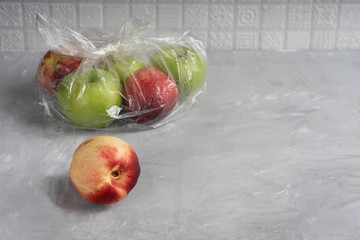 Plastic or polyethylene transparent bag  full of ripe apples and nectarines at kitchen on concrete...