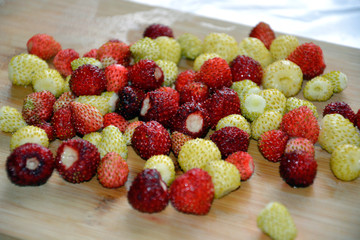 Red and white strawberries are mixed in a heap. Ripe berries lie on the wooden surface.