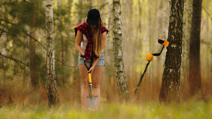 Search with a metal detector. Young woman digging detected metal in the forest. High quality photo