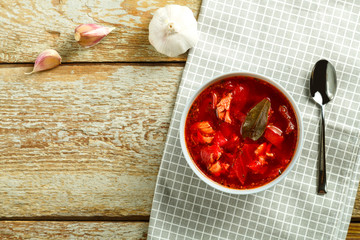 A plate of borscht with chicken on a napkin with a spoon on a wooden table.