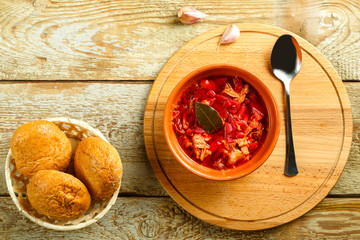 A plate of clay borscht with chicken with a spoon on a wooden table on a round stand next to buns with bran.