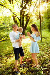 Young family walking at the park, caring parents play with little daughter, smiling, loving dad hold adorable baby girl in arms, enjoy weekend outdoors, parenthood concept