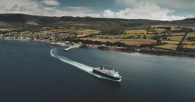 Ferry terminal, Brodick Gulf aerial view. Ship near shore with greenery lands and mountains on horizon. Magnificent seascape with water transportation of Arran Island. Footage shot in 4k, UHD