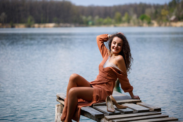 A girl with long wavy curly hair in a long guipure dress barefoot in the summer in a forest on a...