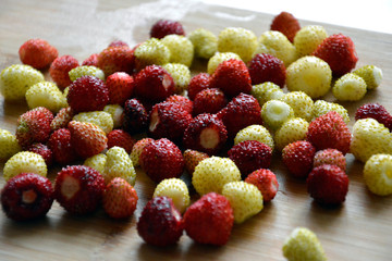 Ripe red and white strawberries are mixed in a pile and lie on a wooden surface.