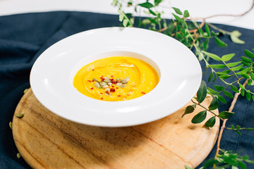 a plate of pumpkin soup garnished with pumpkin seeds. on a dark blue tablecloth. covered with olive branches.