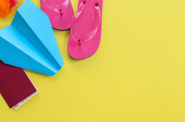 A paper airplane, passport and flip flops lie on the left against a yellow background and with space for text on the right, close-up top view.