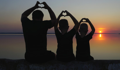 Father and sons sitting on the promenade and look at the river.	Sunset.