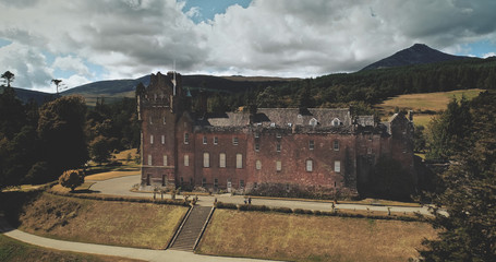 Scotland's Brodick Castle aerial front shot: heritage of Scottish. Historical landmark of Arran Island with majestic landscape. Parks and garden near building under cloudy sky. Scenery view