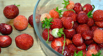 Strawberry berries are close-up on a wooden surface and in a glass bowl. Red and white ripe berries are collected in a container.