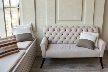 Classic vintage beige buttoned sofa with cushions against wall indoors, copy space. Living room interior