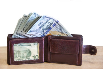 Packs of money are in a wallet that lies on the table near the computer. Money dollars lie in a leather wallet that stands on the table in the office.