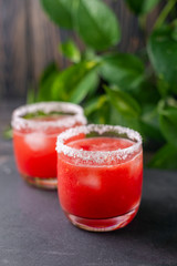Refreshing cold red drink - freshly squeezed watermelon lemonade with ice. Bright juicy non-alcoholic cocktail on a dark wooden background. Idea for a homemade drink recipe. Selective focus
