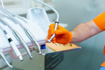 Male dentist's hand in orange gloves working with dental drill machine