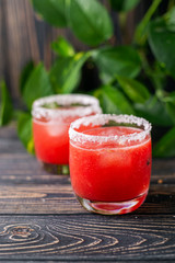 Refreshing cold red drink - freshly squeezed watermelon lemonade with ice. Bright juicy non-alcoholic cocktail on a dark wooden background. Idea for a homemade drink recipe. Selective focus