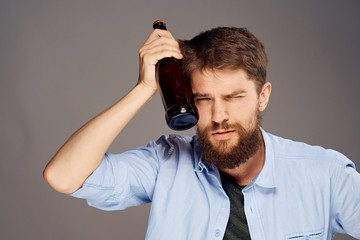 Man with a hangover applies a bottle of beer in his head feeling unwell gray background