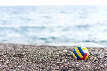 Colored children's ball on a pabble beach on summer sea background. Lonely child's ball forgotten on the beach