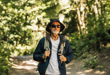 Senior man walking in the forest carrying a backpack