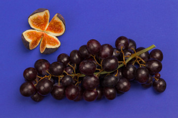 Bunch of black grapes and fig cut into quarters on blue