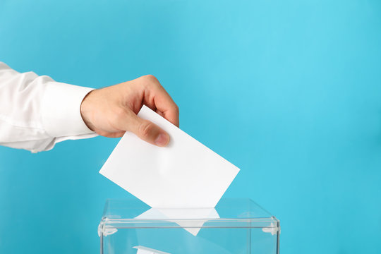 Man putting ballot into voting box on blue background