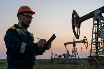 Oil worker checks an oil rig at sunset. Maintenance of oil pump jacks