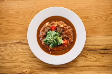 Meat dish with vegetables in white plate on wooden table