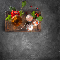 Fototapeta na wymiar Cup of tea and muffins on a wooden board. Viburnum leaves and berries. Flat lay, copy space. Gray background.