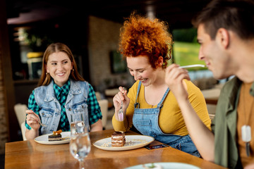 Cheerful redhead woman eating cake with her friends in a cafe.