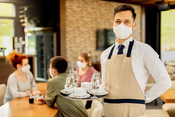 Happy waiter with protective face mask serving customers in a cafe.