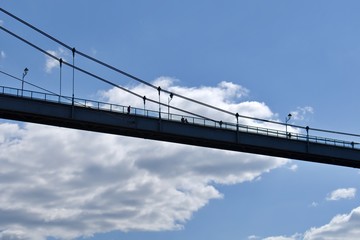 Obraz premium silhouette of footbridge on ropes on blurred background of blue sky with white clouds