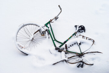 Fototapeta na wymiar Green, abandoned and broken bicycle covered in snow after snowfall.