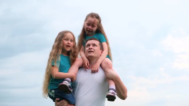 4k. Happy father and two little daughters laughing spending time. Dad and daughters playing together, spinning over blue sky at summer.